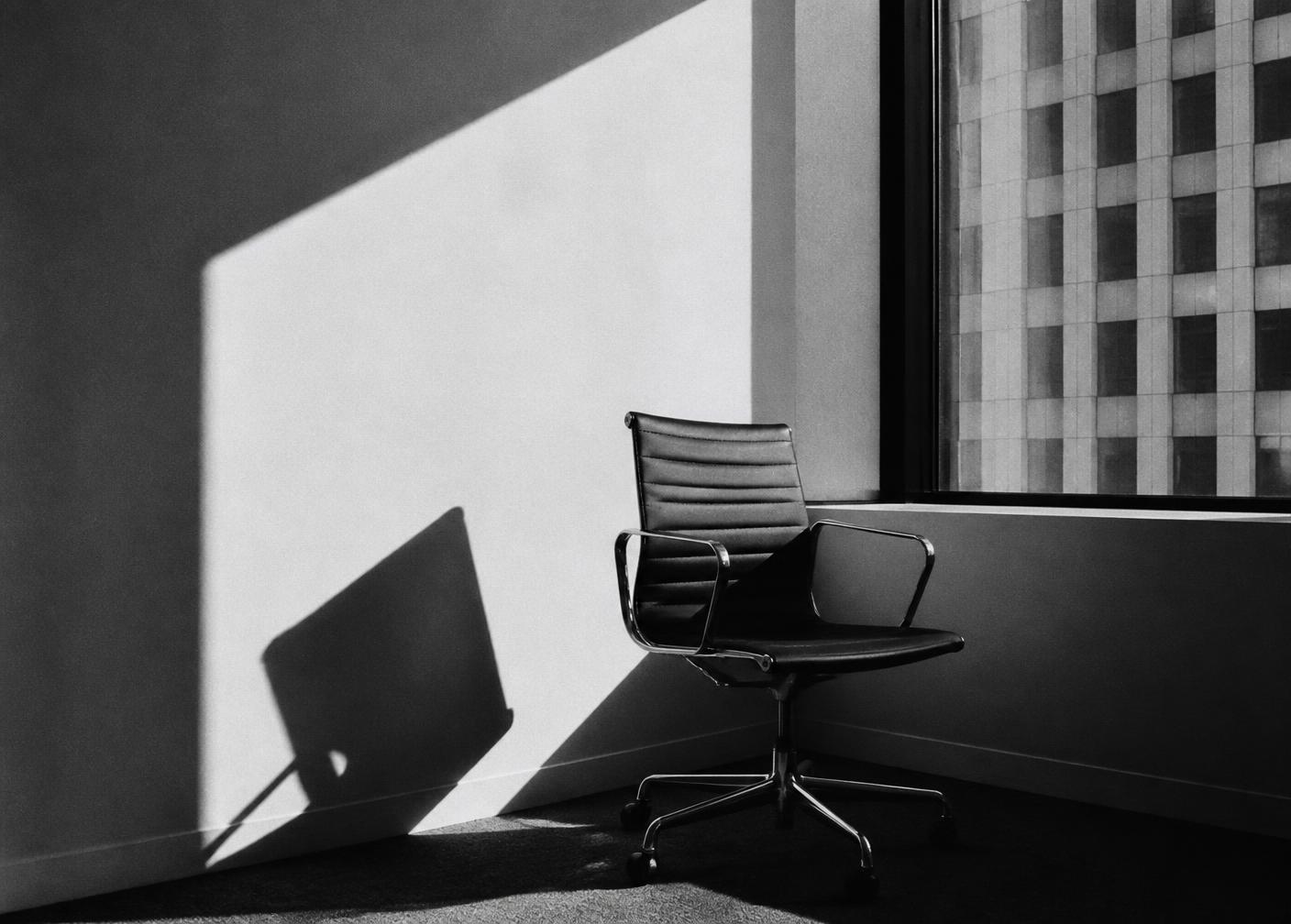 An empty office chair by a window in hard afternoon light